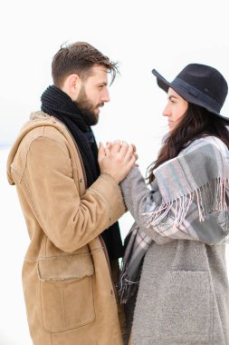 Beyaz arka planda kadın elini tutarak sakallı genç adam eşarp ile bir palto giyiyor portresi.