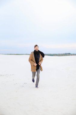 Kahverengi paltonu ve kaşkolünü kar üzerinde çalışan giyen genç şık adam.