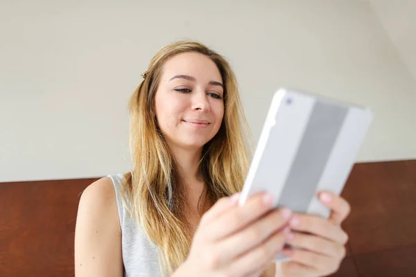 Joven mujer agradable usando tableta para las redes sociales, sentado en la cama . — Foto de Stock