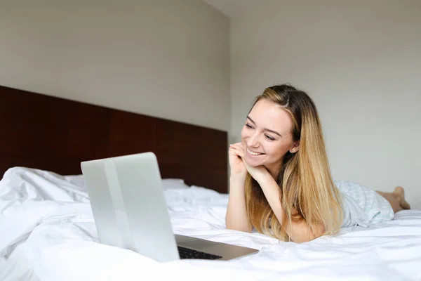 Young woman watching films by laptop and lying on bed in morning on weekends. — Stock Photo, Image