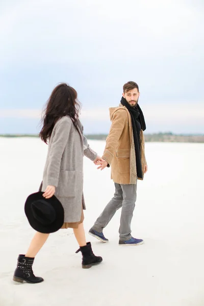 Щасливий чоловік і жінка йдуть на сніг і тримаються за руки, одягнені в пальто і шарфи . — стокове фото