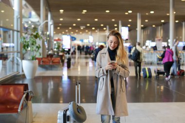 Valiz ile ayakta ve smartphone kullanarak Havaalanı salonundaki kadın.
