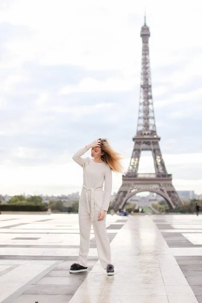 Stylish european woman standing near Eiffel Tower in white overalls. — Stock Photo, Image
