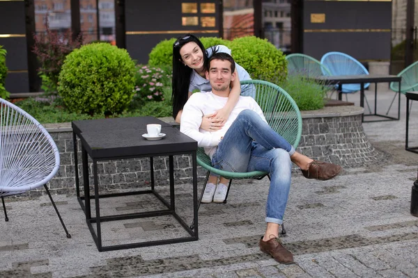 Jovem esposa abraçando marido sentado na cadeira no café de rua fora . — Fotografia de Stock