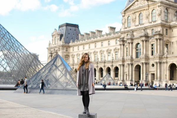백인 여 자가 회색 외 투를 입고 파리의 루브르와 유리 피라미드 근처에 서. — 스톡 사진