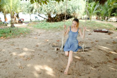 Salıncakta sürme ve kot sundress, arka planda kum giyen genç kız.