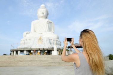 Genç kadın alarak fotoğraf yanında beyaz Phuket Buda heykelinin smartphone.