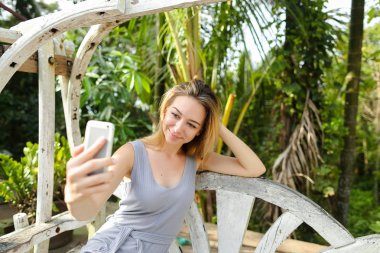 Genç kadın selfie smartphone arka planda salıncakta oturan, avuç içi ile yapma.