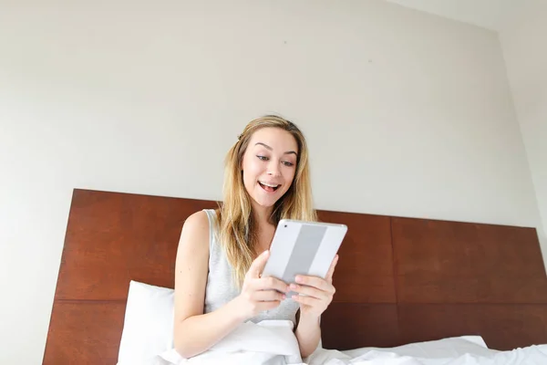 Fiatal nő segítségével tabletta, a szociális hálózatok, ült az ágyban. — Stock Fotó