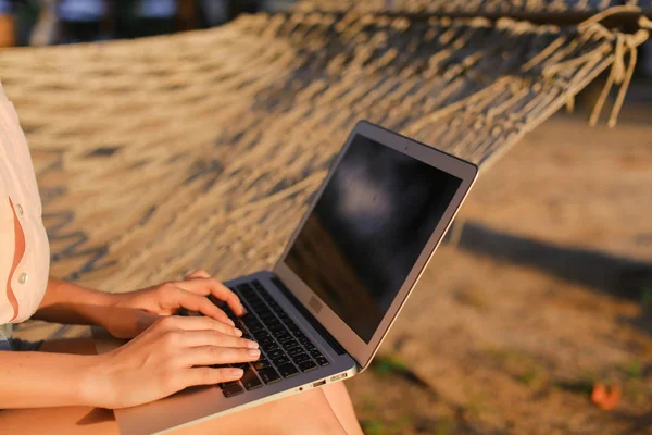 Cerca de persona femenina caucásica usando el ordenador portátil y sentado en hamaca de mimbre . — Foto de Stock