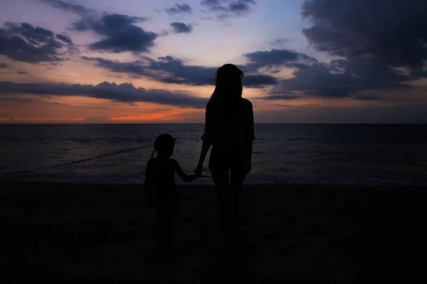 Silhouette nera della persona femminile che cammina con la bambina vicino al mare in fondo al tramonto . — Foto Stock