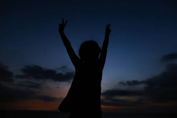 Silueta de niña con las manos extendidas en el fondo del cielo al atardecer . — Foto de Stock