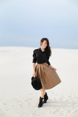 Kar üzerinde duran ve beyaz arka planda kahverengi etek, siyah bluz ve tutma şapka giyen çekici kız.