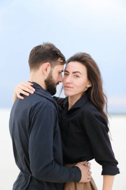 Birbirlerine sarılma ve etek giyen ve şapka tutmak bir kadın beyaz kış arka planda duran genç çift.