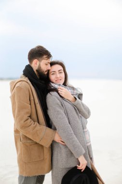 Sakal sarılma kadın kişi giyen gri ceket ve eşarp, Beyaz Kış tek sesli arka plan ile mutlu genç adam.