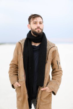 Paltonu ve kaşkolünü beyaz kar arka planda duran giyen sakallı Avrupa Genç erkek kişi.
