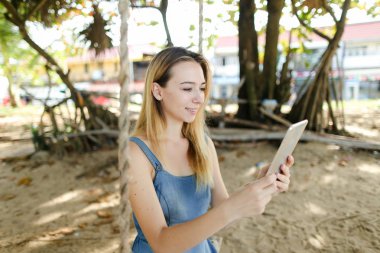 Kot sundress giyen tablet kullanma ve salıncak kum üzerinde sürme kadın genç güzel.