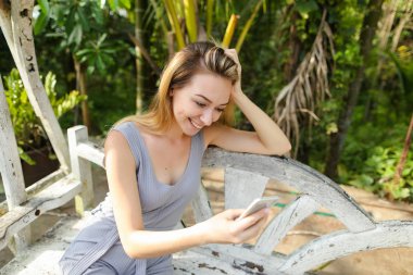 Avuç içinde geçmiş, salıncakta oturan Smartphone kullanan genç gülümseyen kadın.