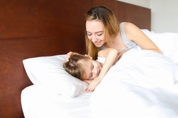 Jovem mulher dormindo com a filhinha de manhã na cama com lençóis brancos . — Fotografia de Stock