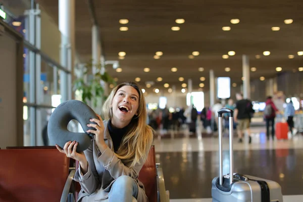 Uśmiechnięta kobieta siedzi z Poduszka pod szyję i bagażu w poczekalni Lotnisko. — Zdjęcie stockowe