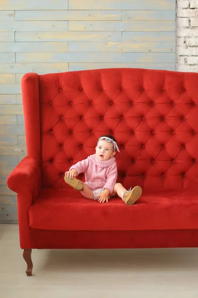 Little caucasian girl sitting on red sofa. — Stock Photo, Image