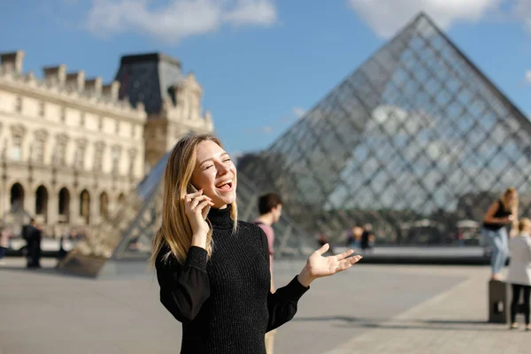 Woman standing near Louvre and glass pyramind in black dress in Paris, talking by smartphone. — Stock Photo, Image