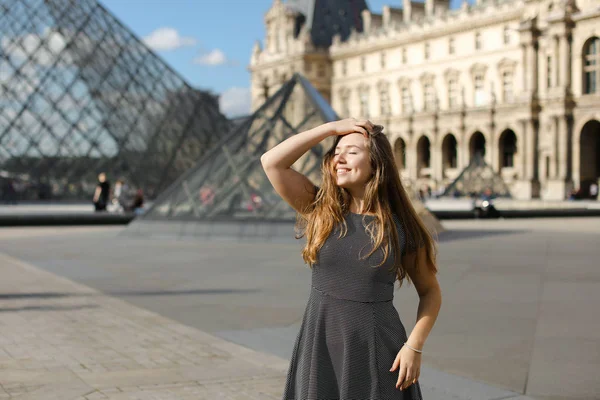 Jonge vrouw staande in de buurt van piramide van het Louvre en glimlachen. — Stockfoto