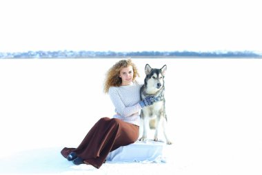 Beyaz kar arka planda husky ile oturan eldivenler giymiş kadın kişi.