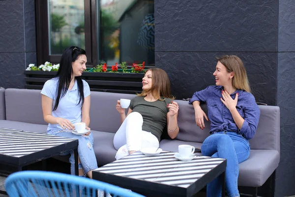 Jóvenes amigas riendo y hablando en la cafetería, tomando café . — Foto de Stock