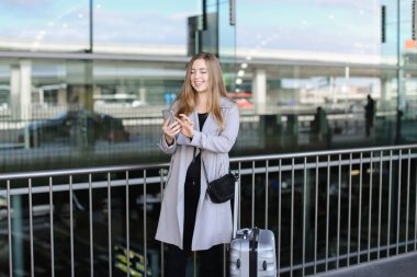 Sohbet ve smartphone valiz ve Havaalanı yakınında tarama genç güzel kadın.