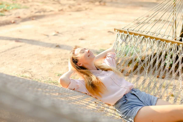 Young caucasian woman lying on white wicker hammock with sand in background. — Stock Photo, Image