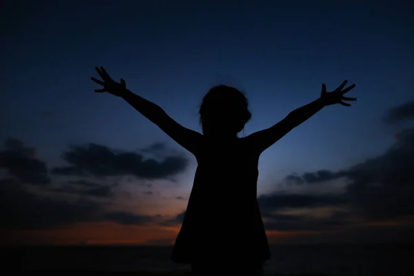 Silueta negra de niña con las manos extendidas en el fondo del cielo al atardecer . — Foto de Stock