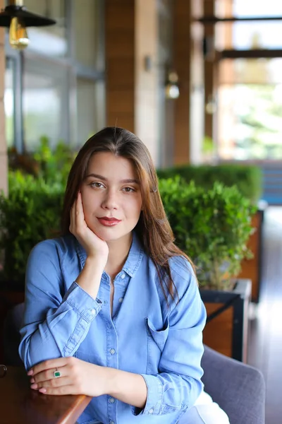 Menina sentada no café inclinada na mão, vestindo camisa jeans — Fotografia de Stock