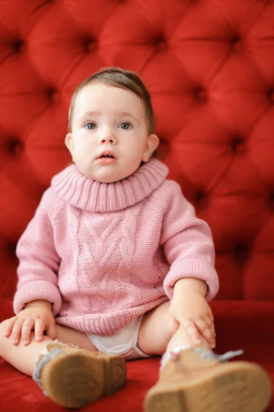 赤い背景のソファの上に座っている素敵な女性赤ちゃん. — ストック写真