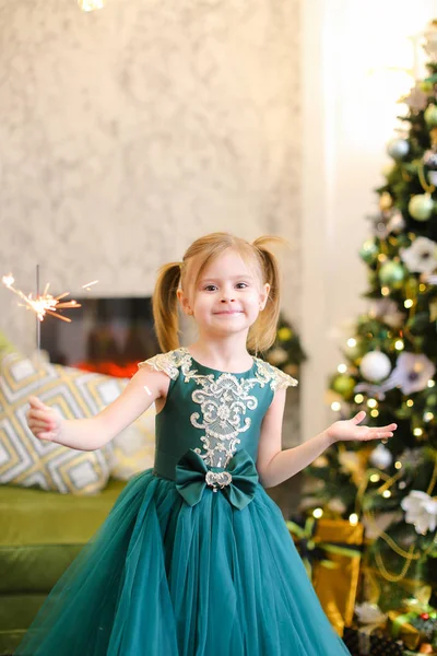Kleines lustiges Mädchen in Kleid und mit Bengalischen Lichtern am Weihnachtsbaum stehend. — Stockfoto