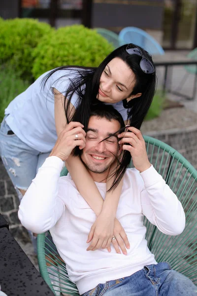 Morena esposa beijando e abraçando marido sentado na cadeira no café de rua fora . — Fotografia de Stock