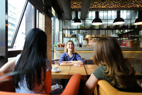 Mujeres sonrientes sentadas en la acogedora cafetería, sonriendo y tomando café . — Foto de Stock