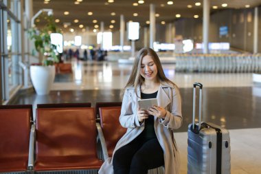 Havaalanı hall yanında valiz tablet ile internet kullanan kadın.