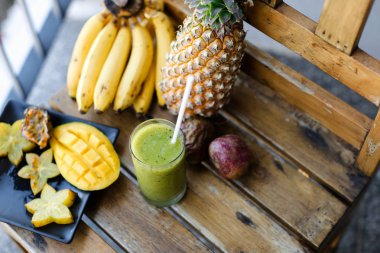 Güzel çam elma muz, carambola ve mango ayakta ahşap sandalye, kivi taze meyve suyu.