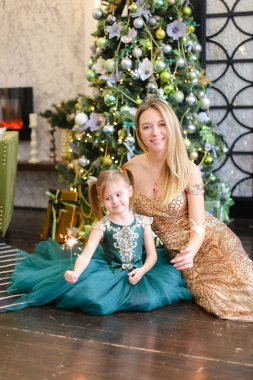 Genç güzel anne ve küçük kızı bengal Noel ağacı yakınındaki katta oturan ışık ile.