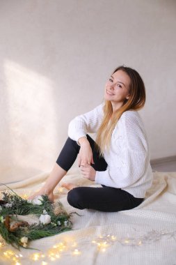 Yatakta çelenk ve sarı çelenk yakın oturan genç beyaz kadın.