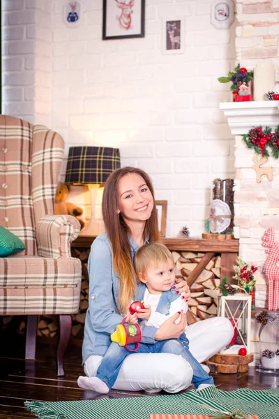 Joven madre sentada con su hijita en habitación decorada para Navidad . — Foto de Stock