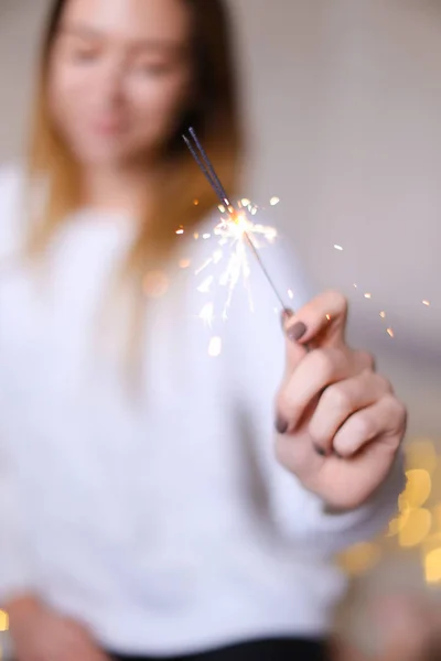 Foto borrada de menina bonita jovem com luz bengala perto de guirlandas amarelas cintilantes . — Fotografia de Stock