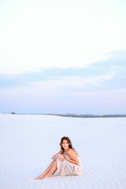 Kum üzerine oturan beyaz Battaniye sarılı beyaz çekici kız