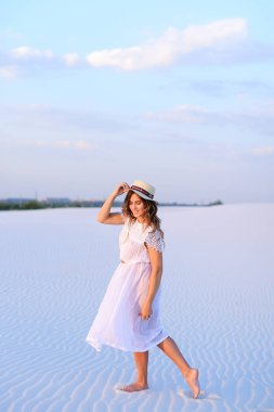 Genç çekici kız beyaz elbise ve şapka üzerinde kum barefoo gidiyor