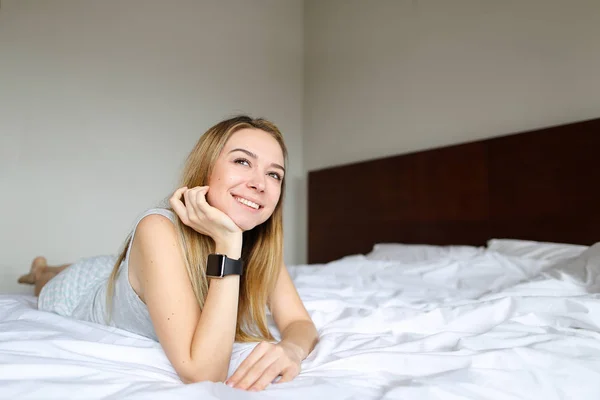 젊은 미소 여자 smartwatch 사용 하 고 아침에 흰색 린 넨 침구와 침대에 누워. — 스톡 사진