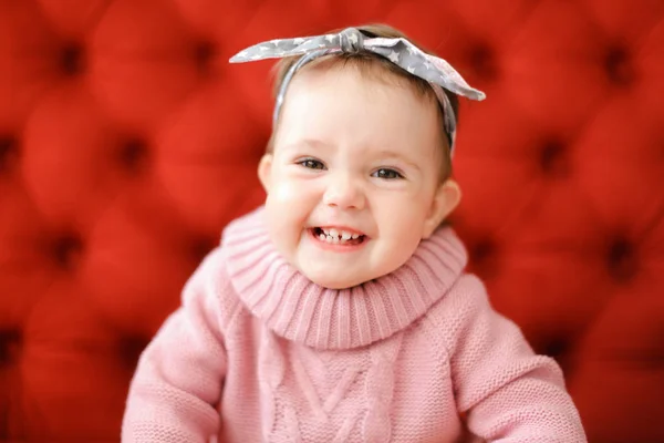 赤い背景に座っているピンクのセーターを着ているクローズ アップ笑みを浮かべて女性赤ちゃん. — ストック写真