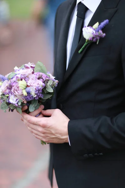Caucasian groom wearing black suit and tie keeping bouquet of flowers. — Stock Photo, Image