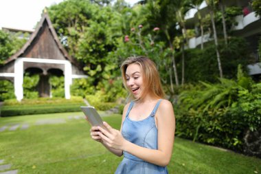 Smartphone kullanarak ve resort ev arka planda duran genç gülümseyen kadın.