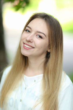 Dışarıda beyaz bluz giyen genç gülümseyen kadın portresi.
